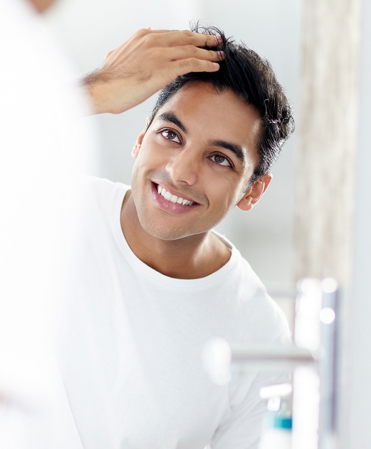 Man styling hair in bathroom mirror.