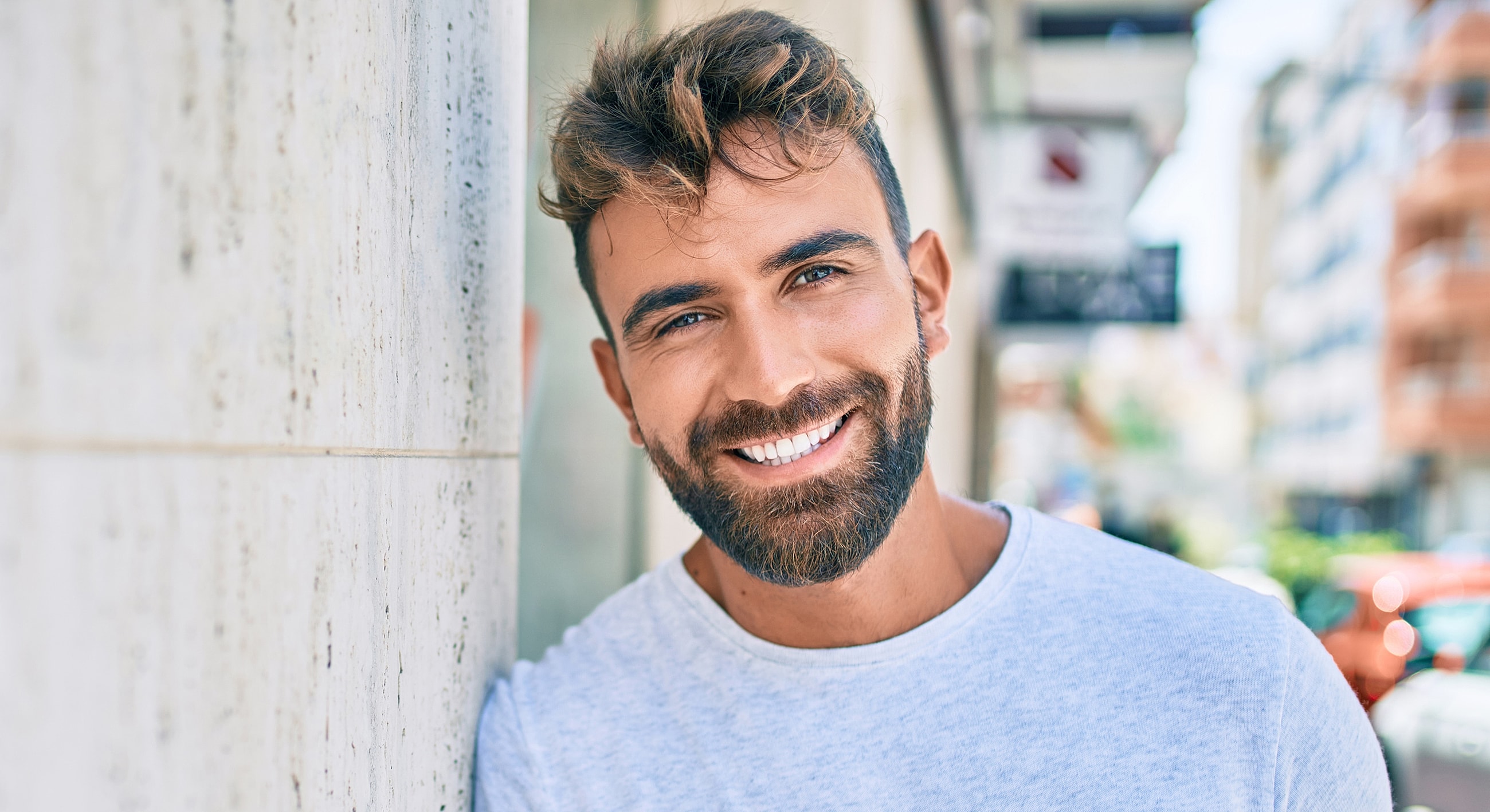 Smiling man leaning against a wall outdoors.